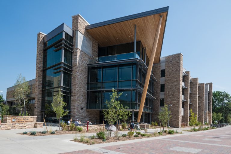 The Michael Smith Natural Resources Addition at Colorado State University, a modern stone and glass building with a prominent wooden overhang and large vertical windows.