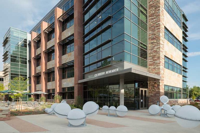 The Chemistry Research Building at Colorado State University, a contemporary structure with glass and stone exterior walls and modern outdoor seating sculptures near the entrance.