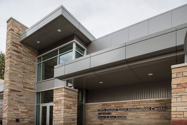 The JBS Global Food Innovation Center at Colorado State University, featuring modern architecture with stone and metal accents and large glass windows at the entrance.