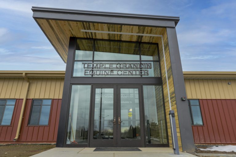 Entrance of the Temple Grandin Equine Center at Colorado State University, featuring modern architecture with glass doors, wood paneling, and a slanted metal roof.