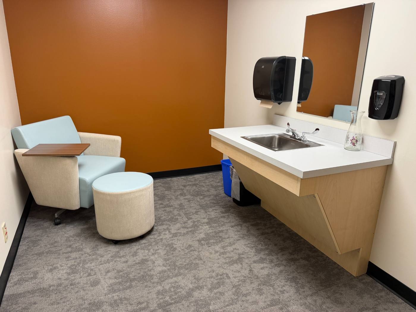 Accessible and inclusive lactation room with movable furniture, roll-under sink, mirror, and soft finishes.