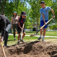 Children helping to dig hole with man for Arbor Day planting
